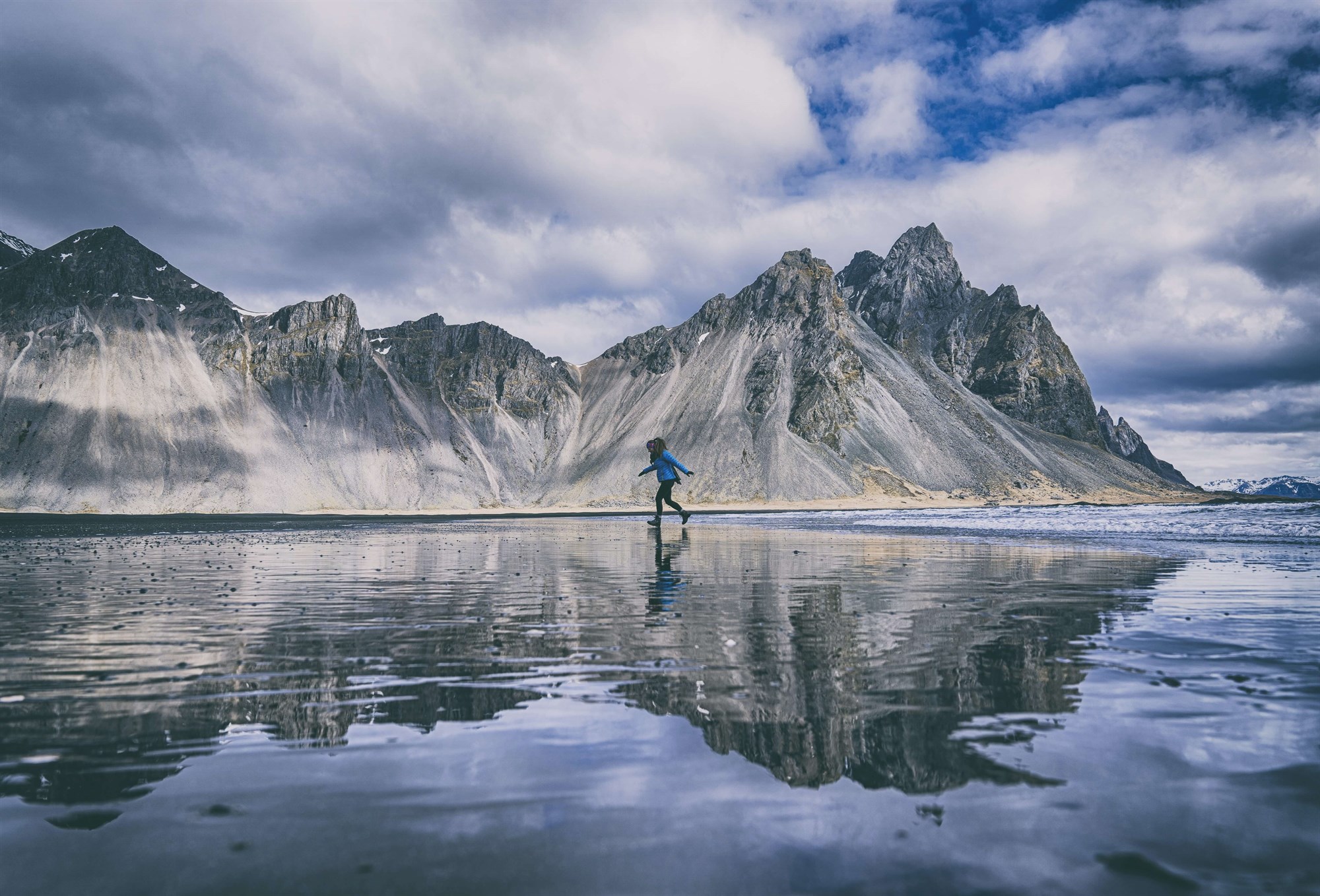 Woman walking along Stokksnes black beach in front of mountains