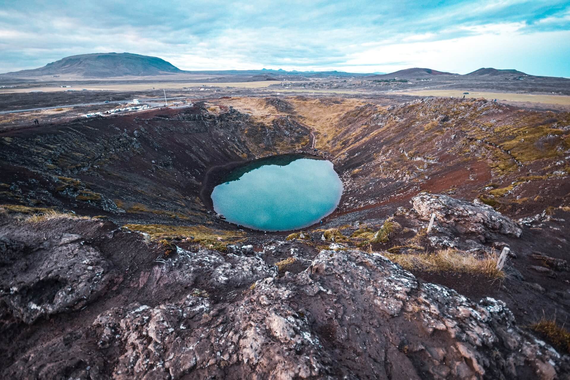 An aerial photograph of the Kerid crater in Iceland showing the icy blue water surrounded by dark volcanic rock