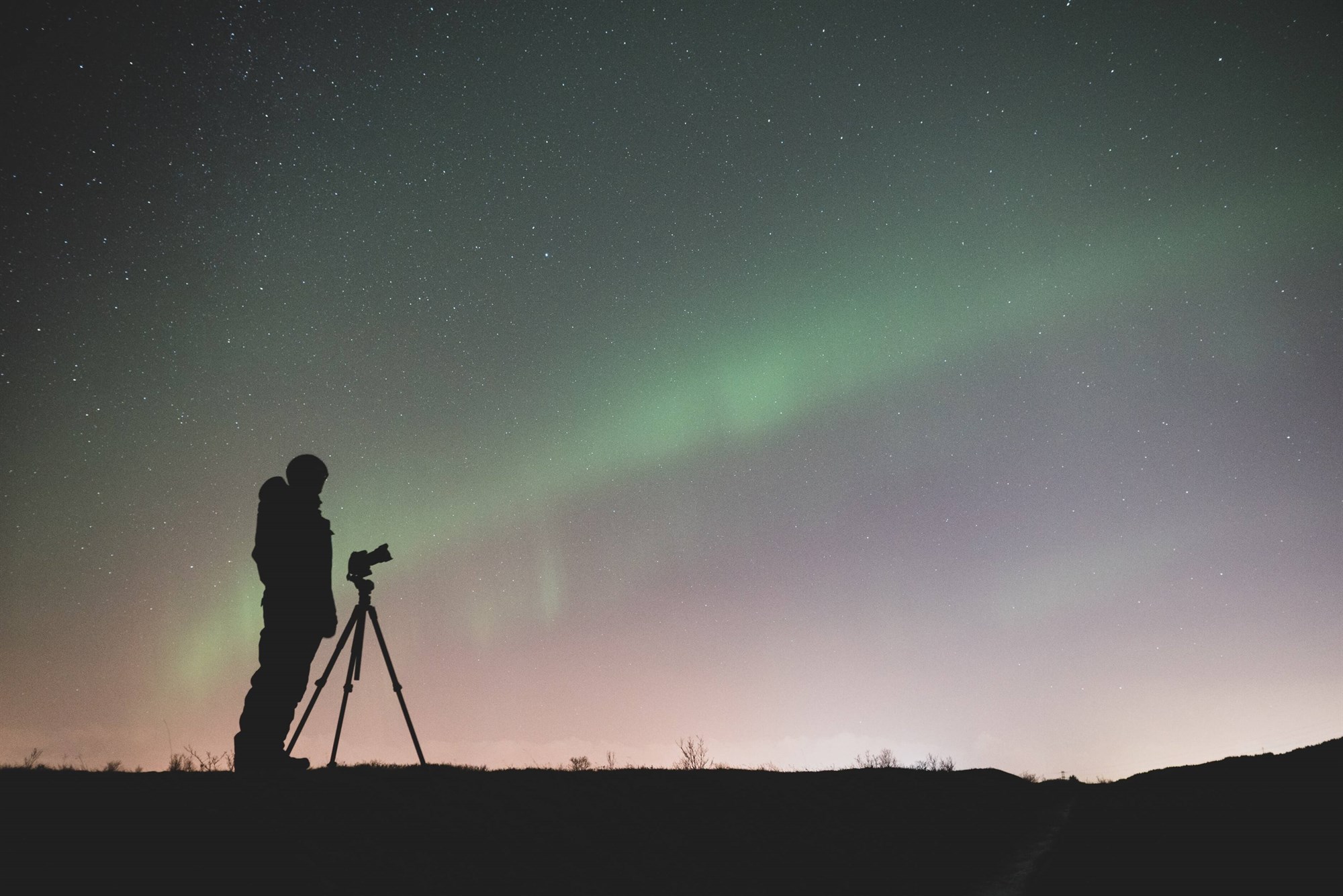 Silhouette of a person with a camera underneath the Northern Lights